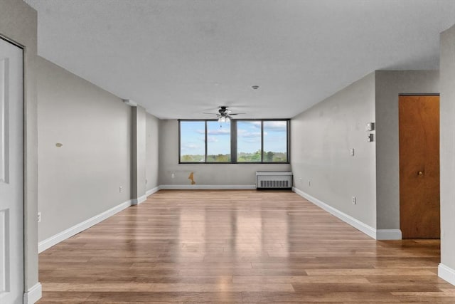 unfurnished living room featuring ceiling fan, radiator, light wood-style flooring, and baseboards