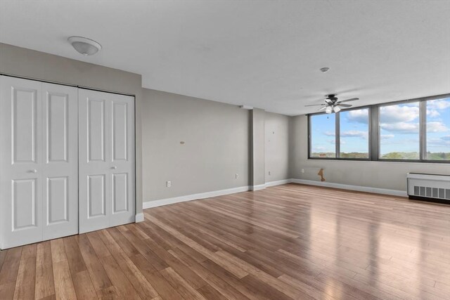 unfurnished living room featuring a ceiling fan, wood finished floors, radiator heating unit, and baseboards