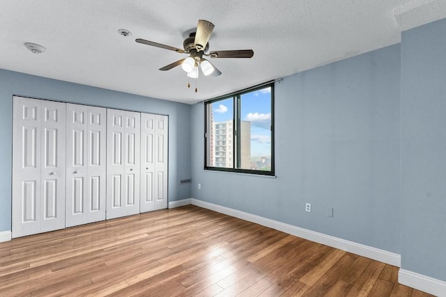 unfurnished bedroom featuring wood finished floors, a textured ceiling, baseboards, a closet, and ceiling fan