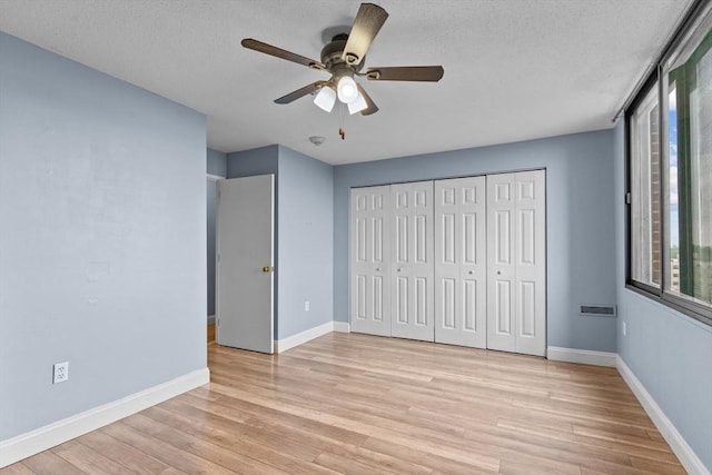 unfurnished bedroom featuring light wood-style floors, baseboards, a textured ceiling, and a closet
