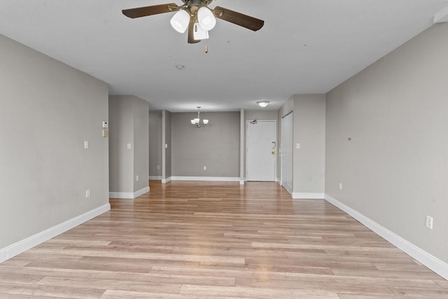 empty room with ceiling fan, a chandelier, light wood-style floors, and baseboards
