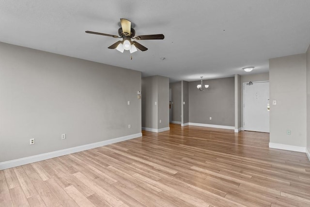 spare room with a chandelier, a ceiling fan, light wood-style floors, and baseboards