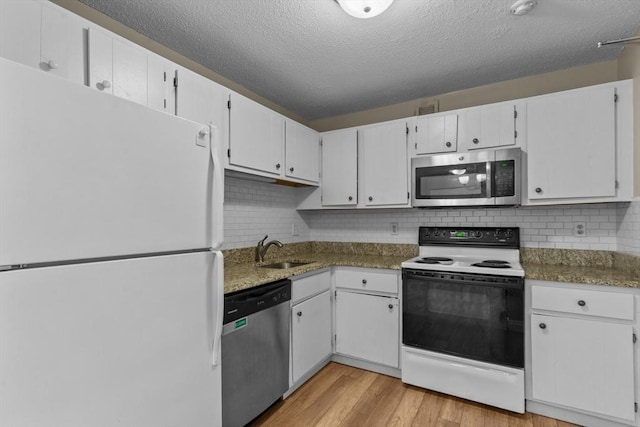 kitchen with appliances with stainless steel finishes, a sink, a textured ceiling, light wood-style flooring, and white cabinetry