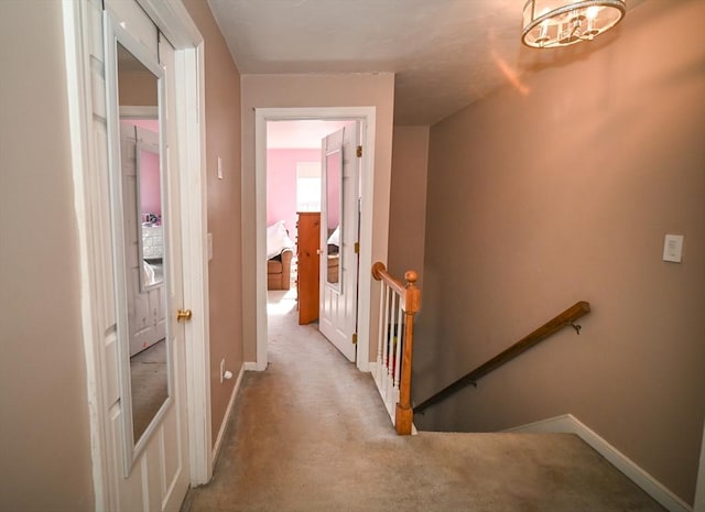 hall with carpet, baseboards, a notable chandelier, and an upstairs landing