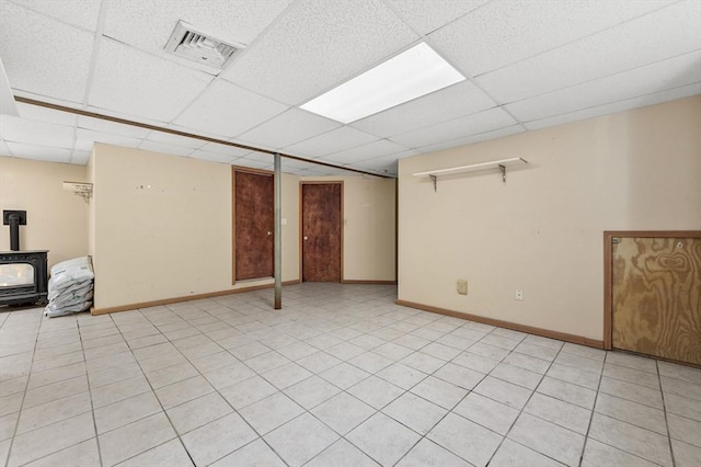 finished below grade area with visible vents, a wood stove, baseboards, and a drop ceiling