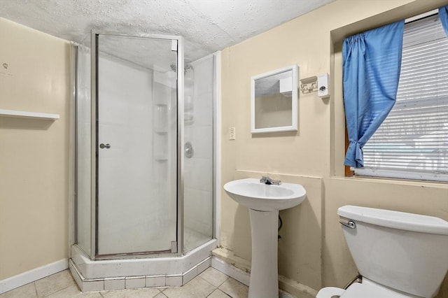 bathroom with a shower stall, baseboards, toilet, tile patterned floors, and a textured ceiling