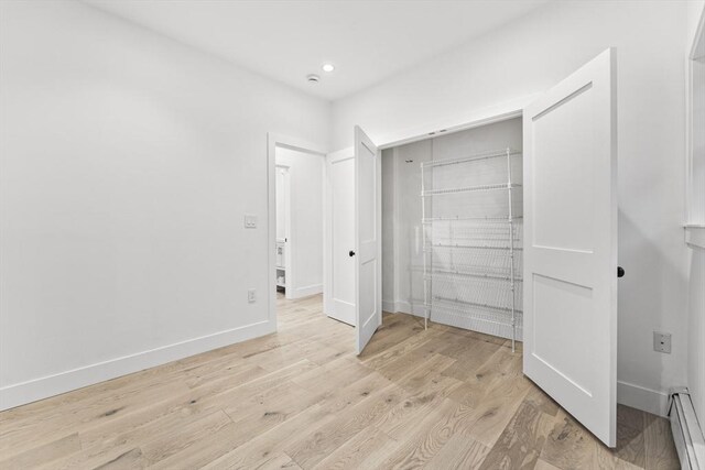 bedroom with a crib, a baseboard radiator, and hardwood / wood-style floors