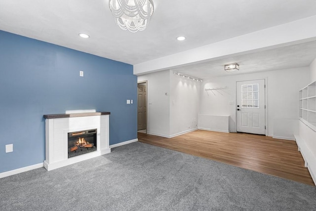 unfurnished living room featuring a warm lit fireplace, carpet flooring, and baseboards