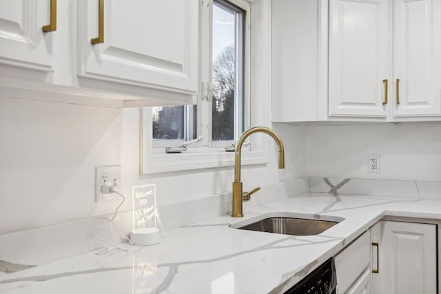 kitchen with dishwasher, white cabinetry, light stone counters, and a sink