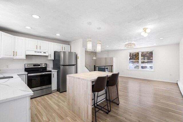 kitchen with pendant lighting, stainless steel appliances, white cabinets, a kitchen island, and under cabinet range hood