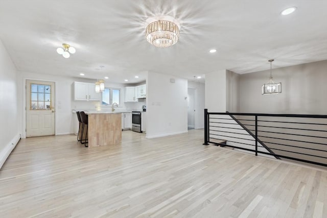 interior space with a notable chandelier, electric range, a kitchen island, white cabinets, and light countertops