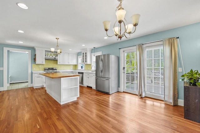 kitchen with appliances with stainless steel finishes, a chandelier, under cabinet range hood, a sink, and white cabinetry
