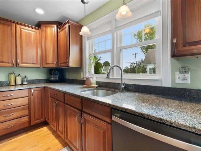 kitchen with sink, hanging light fixtures, stainless steel dishwasher, dark stone counters, and light wood-type flooring