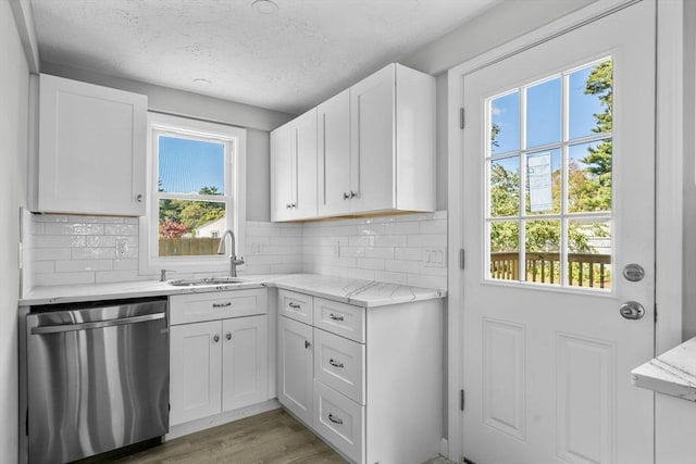 kitchen with white cabinets, light stone countertops, decorative backsplash, dishwasher, and a sink