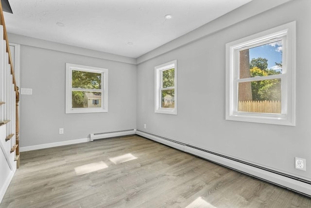 empty room with baseboard heating, a baseboard radiator, wood finished floors, and a healthy amount of sunlight