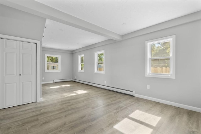 unfurnished bedroom featuring a closet, baseboards, baseboard heating, wood finished floors, and a baseboard heating unit