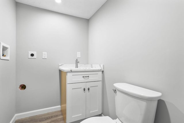 half bath with vanity, baseboards, toilet, and wood finished floors