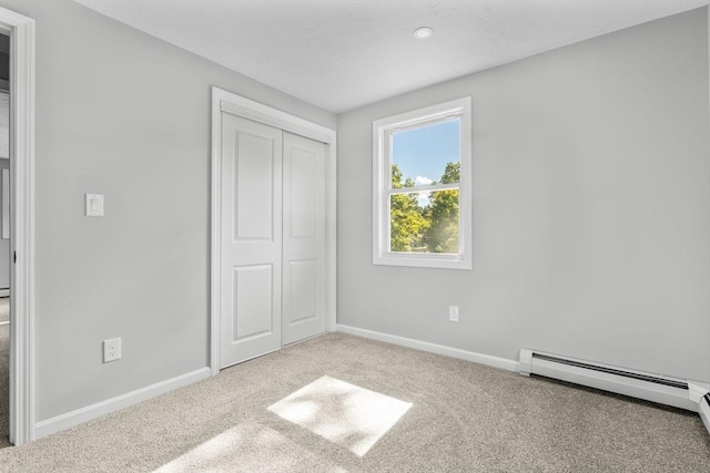 unfurnished bedroom with a closet, a baseboard heating unit, baseboards, and carpet