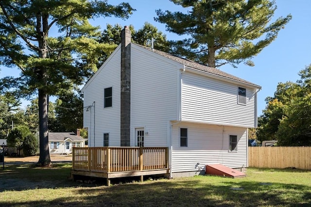 back of property featuring a chimney, fence, a deck, and a lawn