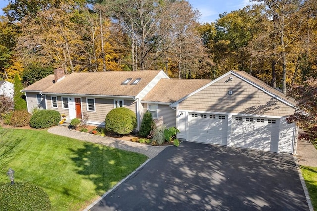 view of front of property featuring asphalt driveway, an attached garage, a chimney, a front lawn, and a shingled roof
