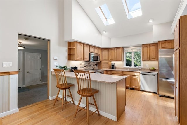 kitchen with stainless steel appliances, a sink, a peninsula, a skylight, and light wood-style floors