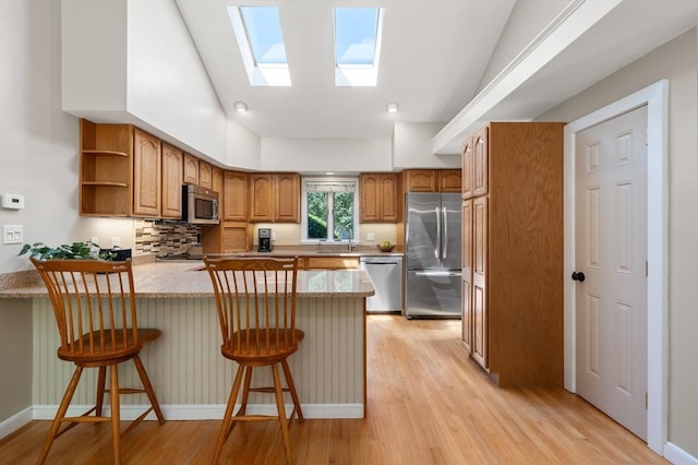 kitchen featuring appliances with stainless steel finishes, a peninsula, a skylight, light wood-style flooring, and open shelves
