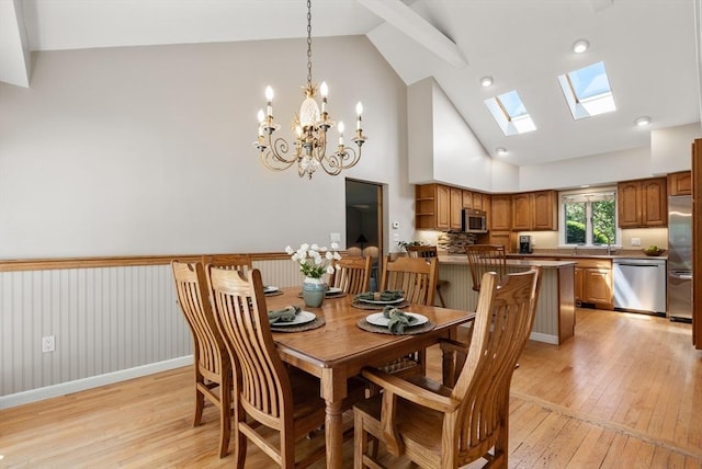 dining area featuring high vaulted ceiling, light wood-type flooring, a skylight, and a chandelier