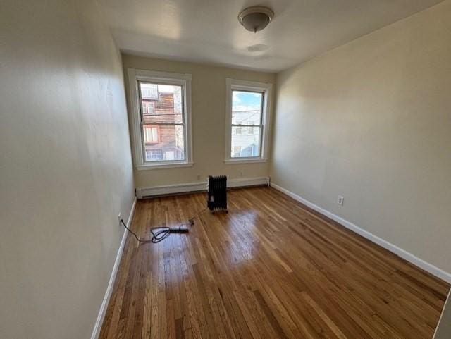 unfurnished room featuring hardwood / wood-style flooring and baseboard heating