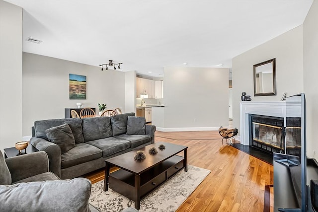 living area with light wood-style floors, a glass covered fireplace, visible vents, and baseboards