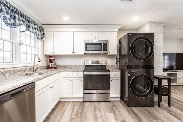 kitchen with stacked washing maching and dryer, appliances with stainless steel finishes, sink, white cabinets, and light hardwood / wood-style flooring