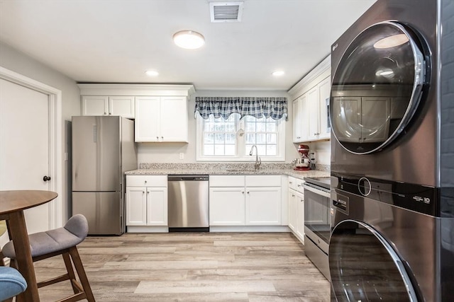 kitchen with stacked washer and clothes dryer, sink, light wood-type flooring, stainless steel appliances, and white cabinets