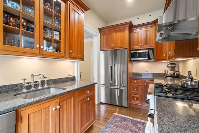 kitchen with wall chimney exhaust hood, appliances with stainless steel finishes, brown cabinetry, and a sink