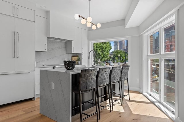 kitchen featuring a kitchen bar, paneled refrigerator, pendant lighting, and white cabinetry