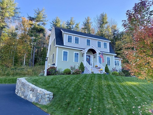 dutch colonial featuring a gambrel roof, a shingled roof, and a front lawn