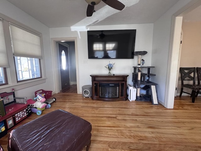 living room featuring a glass covered fireplace, wood finished floors, baseboards, and ceiling fan