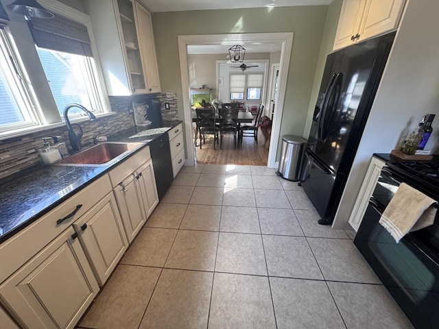 kitchen featuring black appliances, a sink, backsplash, light tile patterned floors, and glass insert cabinets