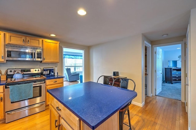 143 Eagle St, Ware, MA 01082 - kitchen with stainless steel appliances, a kitchen breakfast bar, light wood-type flooring, a kitchen island, and dark countertops