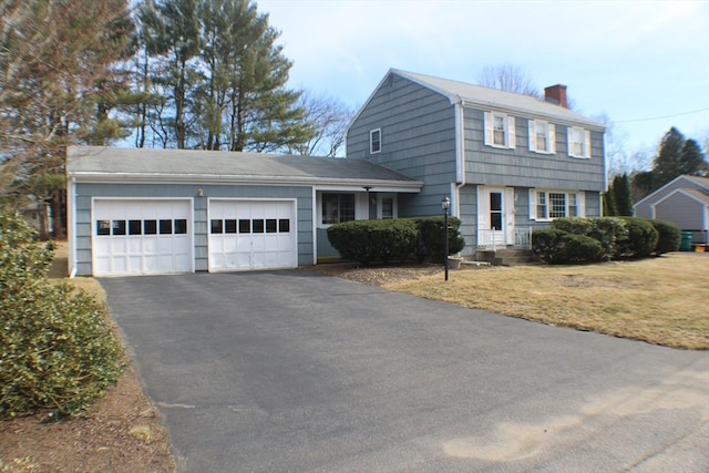 colonial inspired home featuring driveway, a chimney, a garage, and a front yard