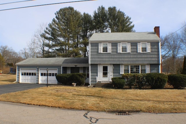 colonial-style house featuring aphalt driveway, a chimney, a front yard, and a garage