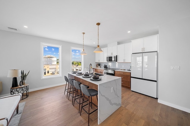 kitchen with appliances with stainless steel finishes, sink, decorative light fixtures, white cabinets, and an island with sink