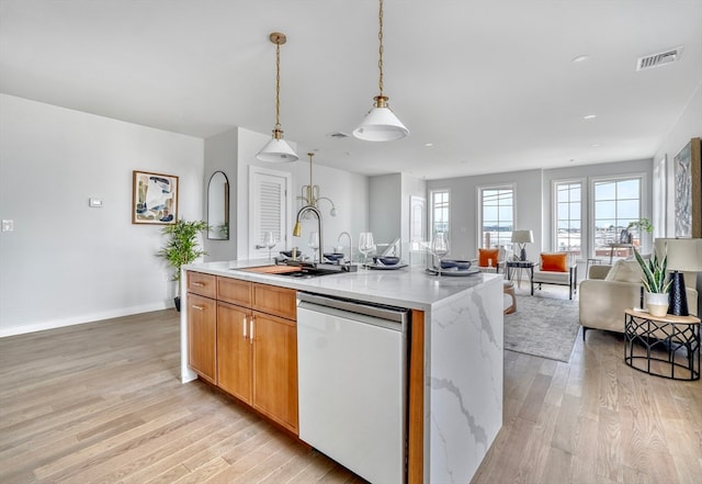 kitchen with light stone countertops, stainless steel dishwasher, sink, light hardwood / wood-style flooring, and an island with sink