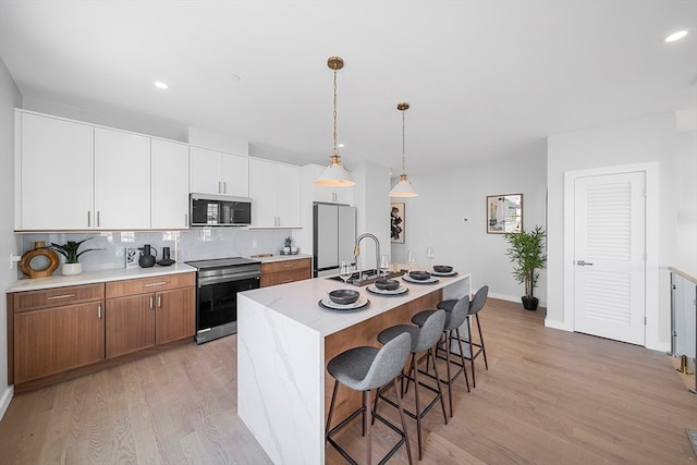 kitchen featuring stainless steel appliances, light hardwood / wood-style flooring, backsplash, a kitchen island with sink, and white cabinets