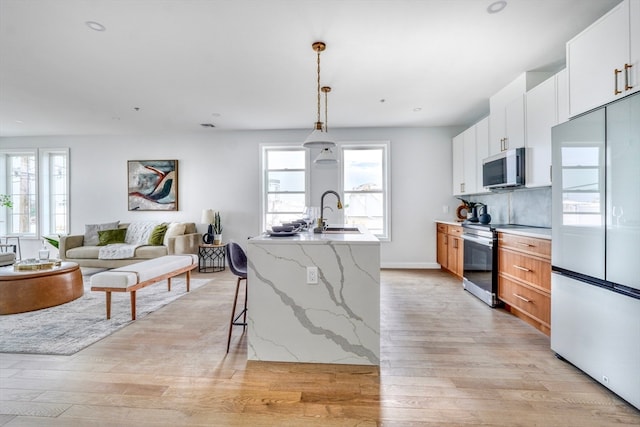 kitchen with appliances with stainless steel finishes, light stone counters, pendant lighting, a center island with sink, and white cabinets