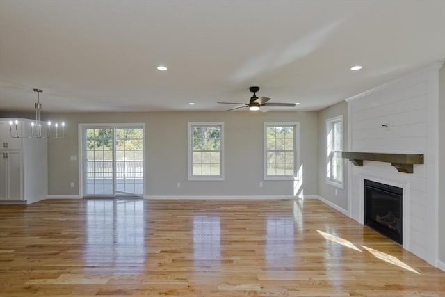 unfurnished living room featuring baseboards, plenty of natural light, ceiling fan with notable chandelier, and light wood-style flooring