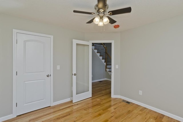 spare room featuring a ceiling fan, visible vents, stairway, baseboards, and light wood finished floors