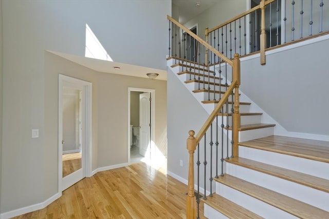 staircase with baseboards, wood finished floors, and a high ceiling