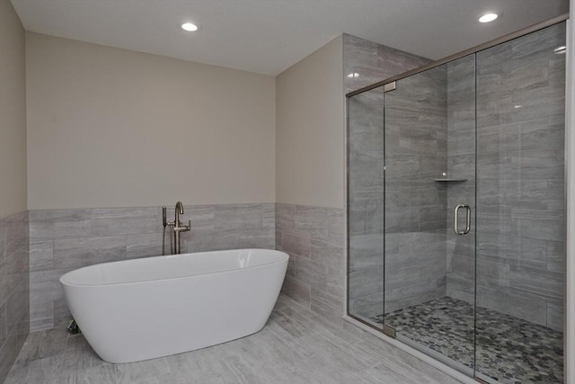 full bathroom featuring tile walls, wainscoting, a stall shower, a soaking tub, and recessed lighting