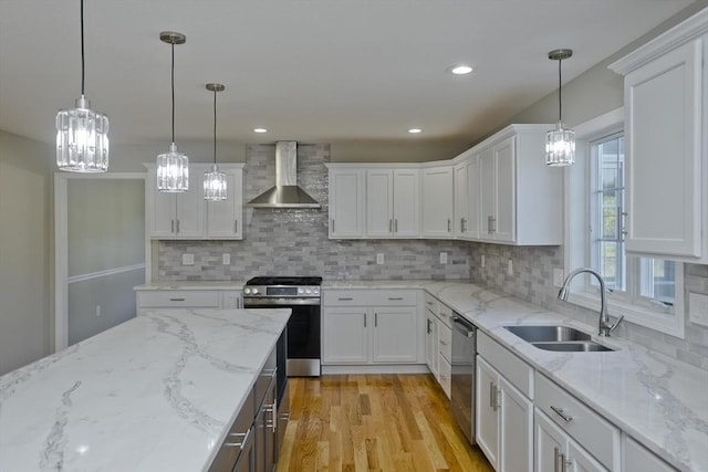 kitchen featuring wall chimney range hood, appliances with stainless steel finishes, an inviting chandelier, a sink, and white cabinetry