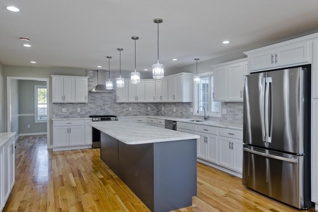 kitchen with wall chimney range hood, white cabinetry, appliances with stainless steel finishes, and a sink