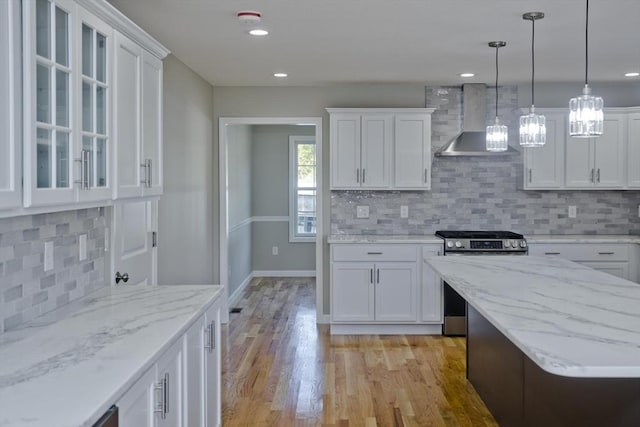 kitchen with wall chimney exhaust hood, gas range, and white cabinetry